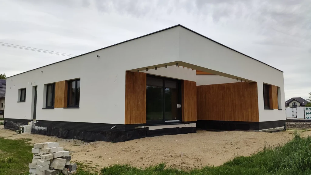 Budynek w stanie deweloperskim, ciemna stolarka okienna, jasna elewacja i elementy okładzina imitująca drewno 