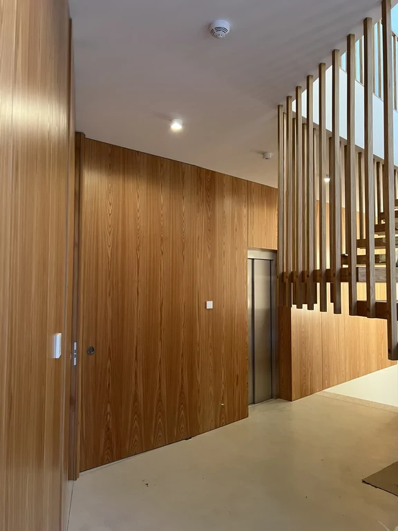 Winda i drewniana okładzina ścienna przy klatce schodowej w minimalistycznym wnętrzu