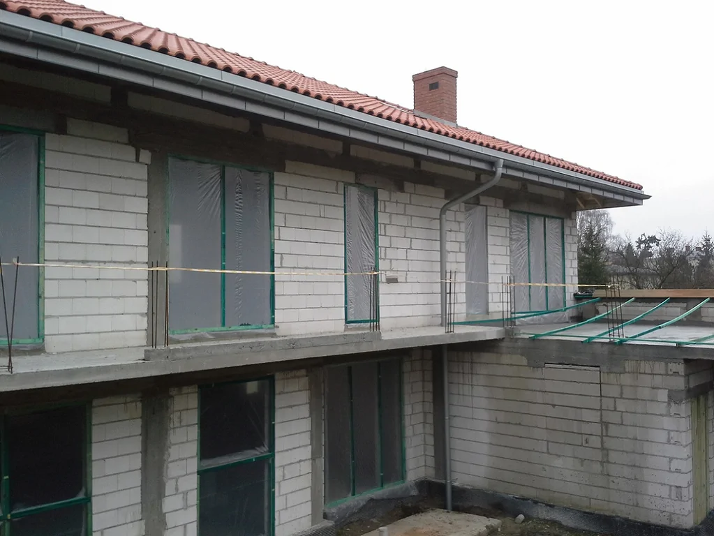 Budowa Domu jednorodzinnego widok z zewnątrz, wykonane mury oraz elementy konstrukcyjne; gotowy dach zaślepione otwory okienne