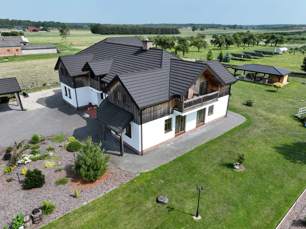Widok z drona na dom od strony ogrodu pod kątem; w tle widoczne elementy zagospodarowania działki i otwarte pola