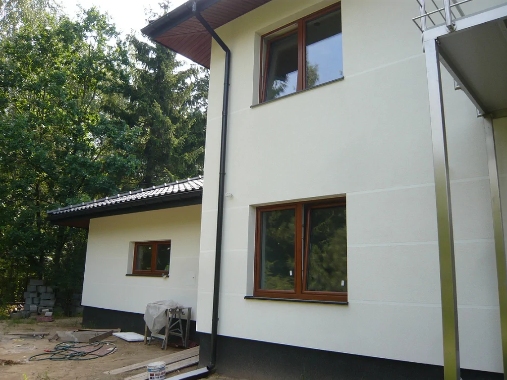 Detal elewacji i dachu – szeroki okap, rynna i brązowa stolarka okienna