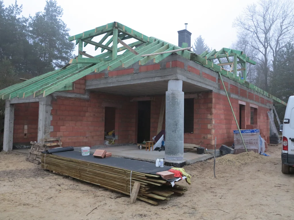 Budowa domu w stanie surowym, cegły Porotherm na ścianach, wykonana więźba dachowa, okrągła kolumna w strefie wejścia