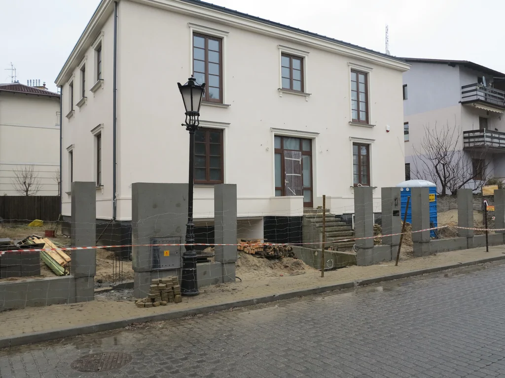 Dom jednorodzinny w stanie deweloperskim, biała elewacja, ciemna stolarka okienna, ogrodzenie żelbetowe