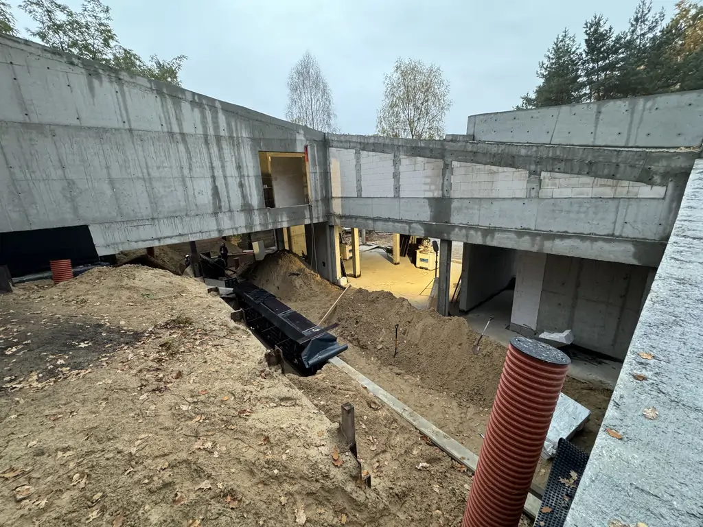 Widok na wewnętrzny dziedziniec budynku w stanie surowym z wykopem i otwartą przestrzenią parteru.