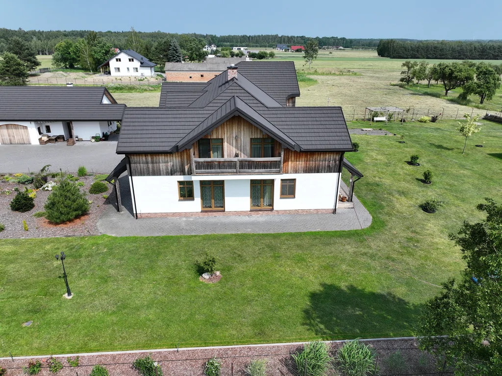 Widok z drona na tylną elewację domu z balkonem nad drzwiami tarasowymi oraz rozległy trawnik