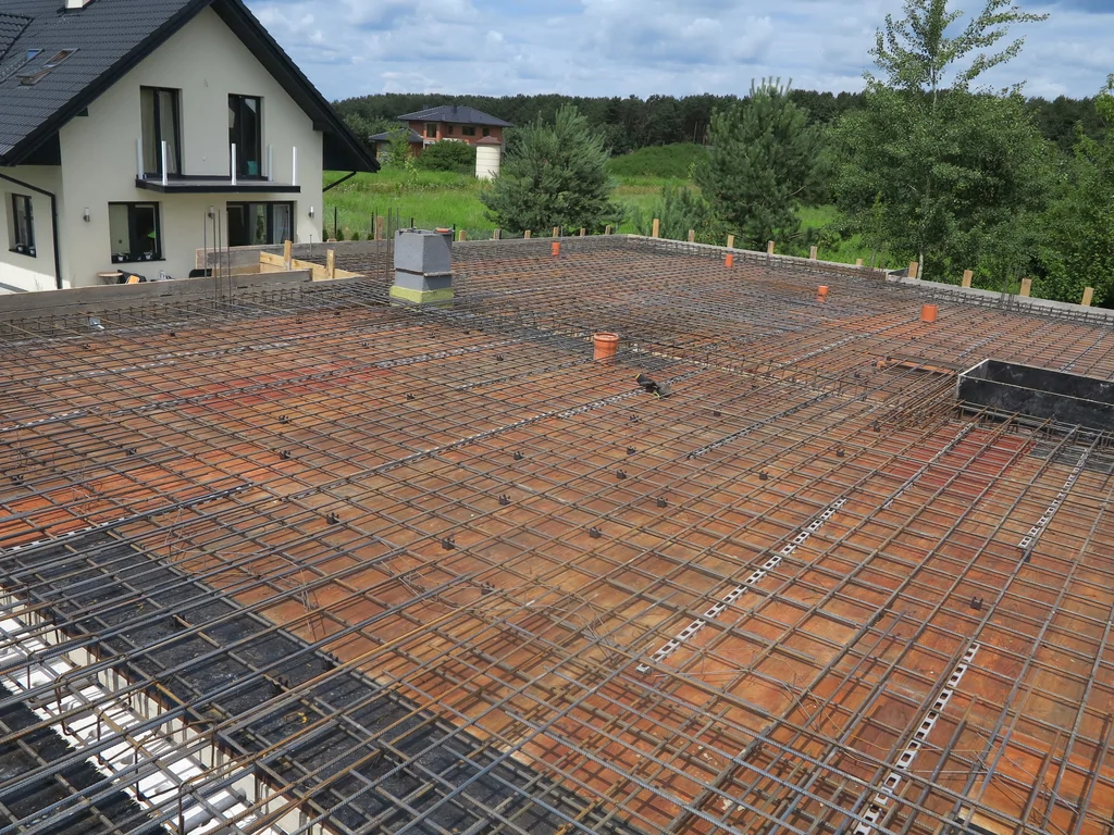 Zbrojenie stropu piętra na budowie domu, w tle inny dom i drzewa