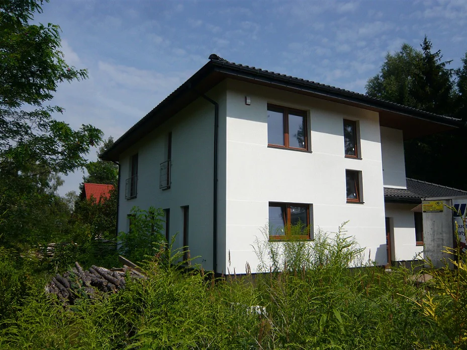 Widok domu od strony ogrodu – jasna elewacja, ciemny cokół i dobudowana część parterowa