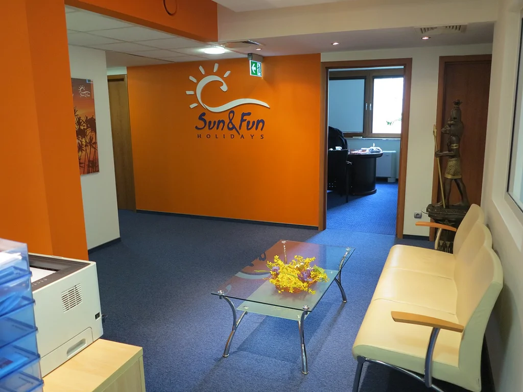 Odnowione pomieszczenie biurowe, widoczny stolik kanapa drukarka, logo biura podróży i artefakty z egiptu