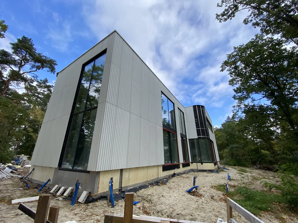 Widok na boczną elewację nowoczesnego domu z wysokim narożnym przeszkleniem, dużymi oknami i zaokrąglonym szklanym narożnikiem