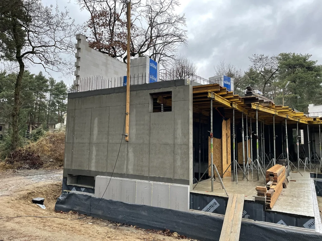 Boczna elewacja domu jednorodzinnego w stanie surowym z żelbetową konstrukcją piwnicy i stropem nad parterem