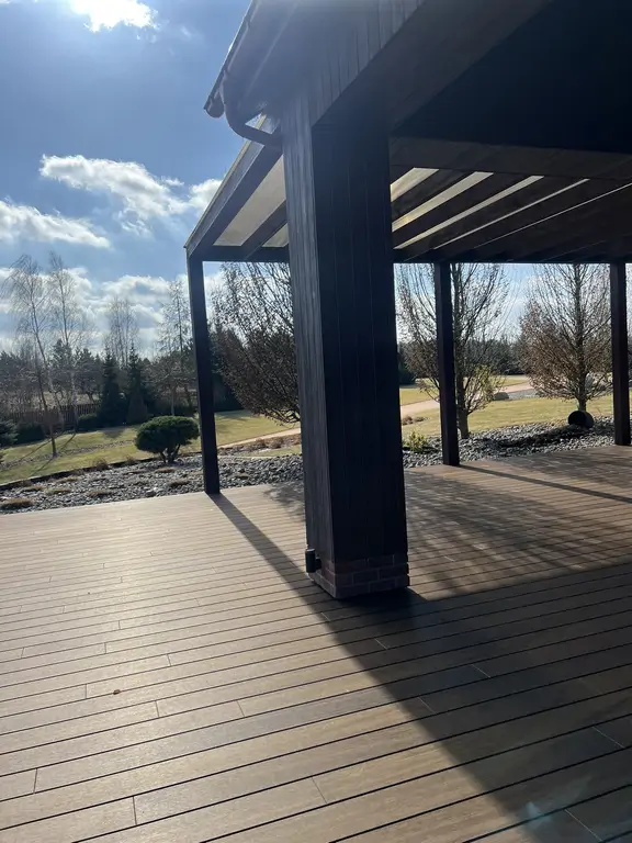 Narożnik wyremontowanego tarasu z zadaszeniem, drewnopodobną podłogą i otwartym widokiem na ogród oraz niebo.