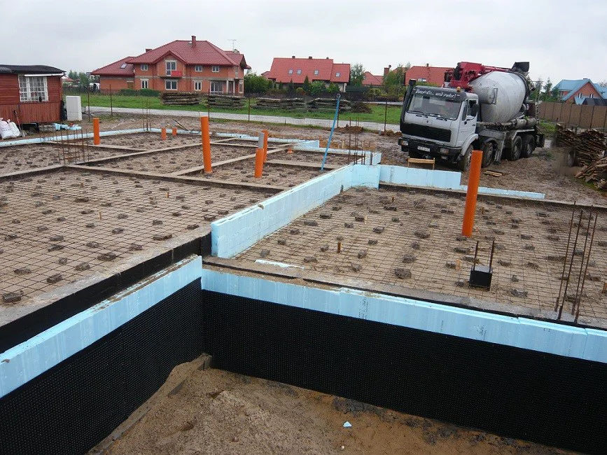 Zbrojenie posadzki fundamentowej oraz izolacja XPS i hydroizolacja; w tle betoniarka (gruszka)