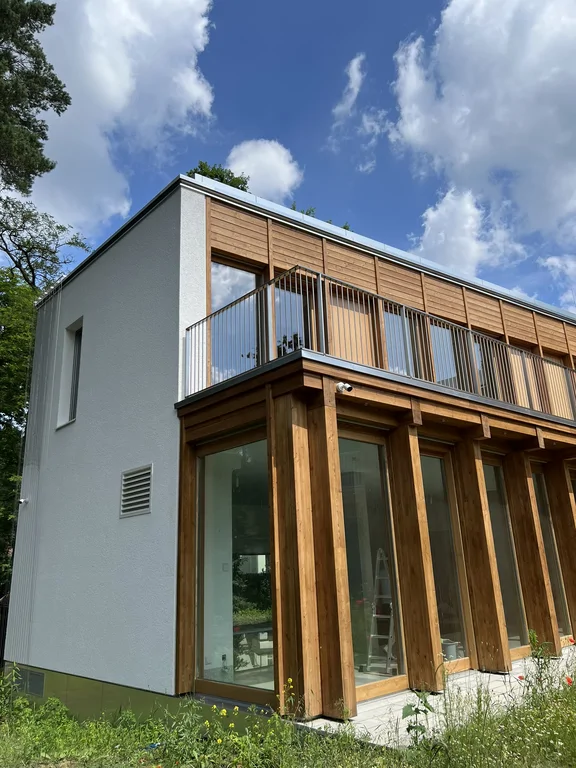 Narożnik nowoczesnego domu z białą ścianą, drewnianą elewacją i tarasem na piętrze