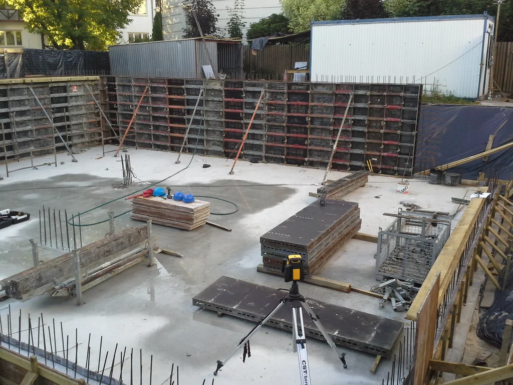 Budowa domu jednorodzinnego, widok na wylaną płytę piwnicy i szalowanie ścian fundamentowych piwnicy w technologii białej wannny