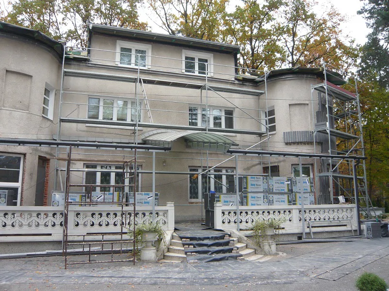 Elewacja frontowa w trakcie remontu; rusztowania i materiał ociepleniowy przy wejściu