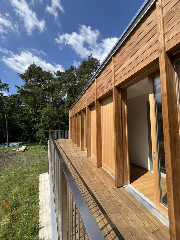 Balkon na piętrze przy drewnianej elewacji z dużymi przeszkleniami i otwartymi drzwiami tarasowymi