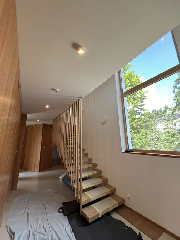 Klatka schodowa z drewnianymi stopniami, ażurową balustradą i dużym oknem