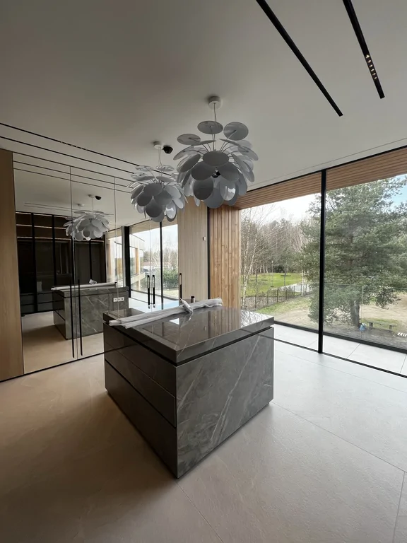 Ujęcie pokazuje relację wyspy z dużym przeszkleniem i drewnem na ścianach. Przestrzeń zaprojektowana pod mocny efekt wizualny.