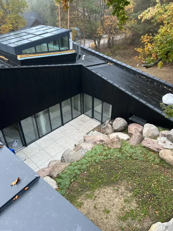 Boczna elewacja nowoczesnej willi z czarną deską elewacyjną, kamiennym cokołem i wysokimi przeszkleniami.