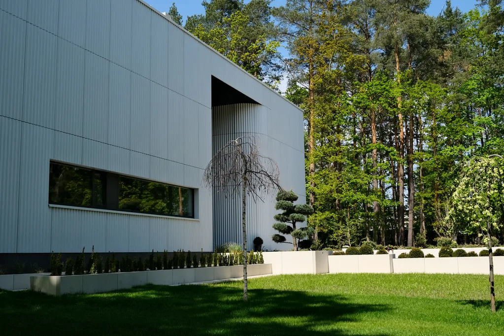 Fragment frontowej elewacji nowoczesnego domu z poziomym oknem, cofniętym wejściem i ogrodem przed budynkiem