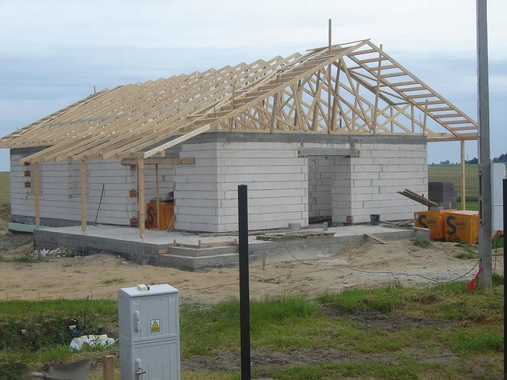 Dom jednorodzinny w trakcie budowy z wymurowanymi ścianami i montażem wiązarów dachowych