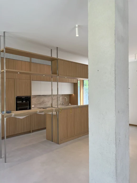 Kuchnia z drewnianą zabudową i wyspą widoczna zza betonowego słupa