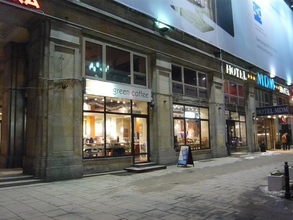 Fasada lokalu Green Caffè Nero z witrynami i szyldem przy Hotelu MDM nocą