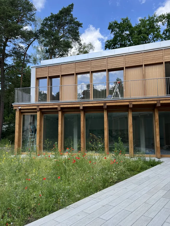 Nowoczesna elewacja domu z drewnianym wykończeniem, wysokimi oknami i tarasem nad dziedzińcem