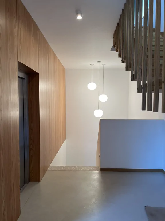 Półpiętro z windą, drewnianą okładziną ścian i schodami z kulistymi lampami wiszącymi