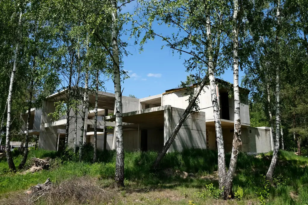 Nowoczesny dom z betonu architektonicznego na etapie konstrukcyjnym, pokazany w naturalnym leśnym krajobrazie.