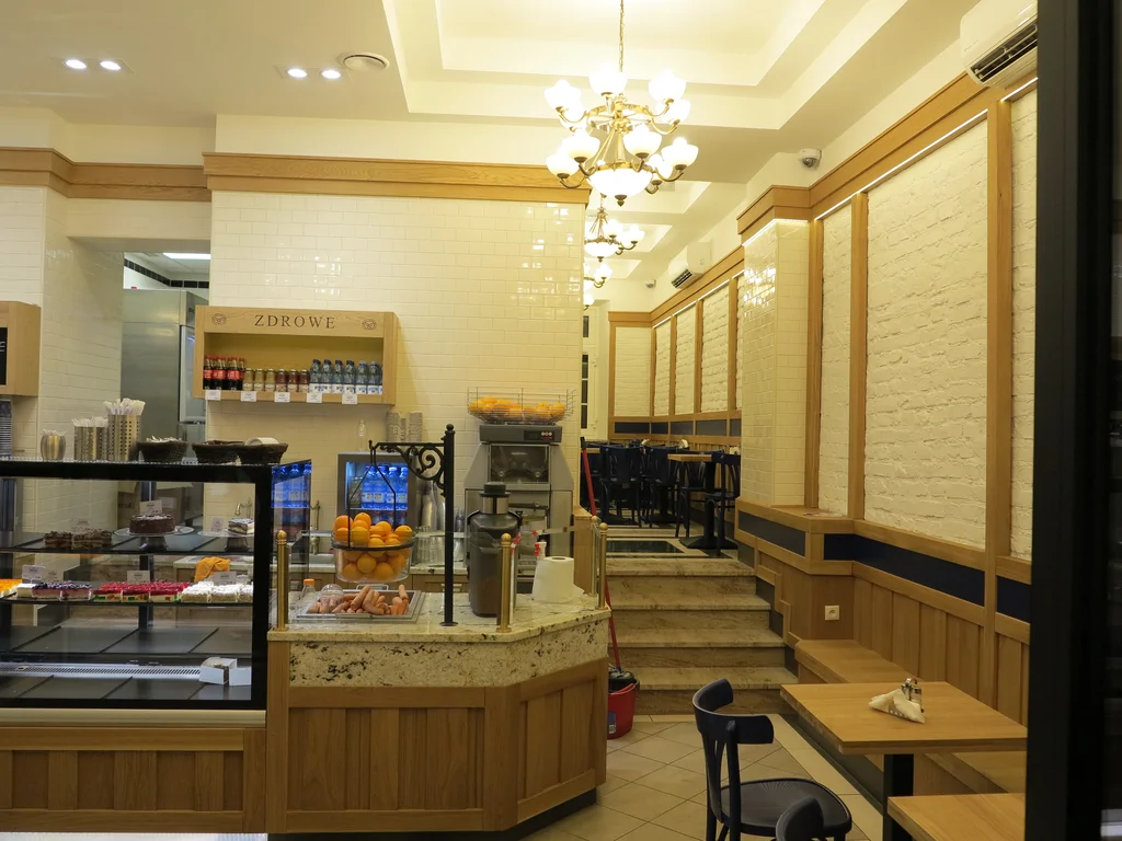 zdjęcie piekarni wewnątrz, kasa, półki z pieczywem, w tle widach kilku stopniowe schodki, na ścianach kamień i drewno 