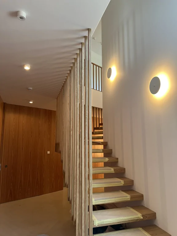 Schody z drewnianymi stopniami, pionowymi lamelami i subtelnym oświetleniem ściennym