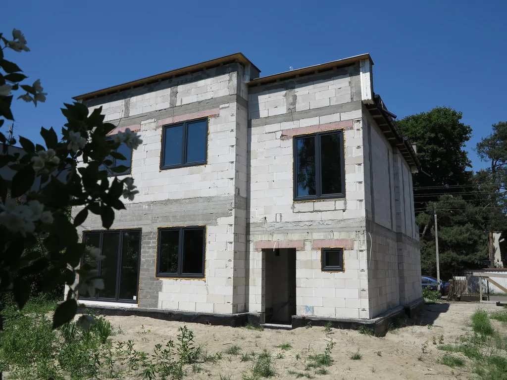 Widok na dom w stanie surowym zamkniętym ze stolarką okienną w ciemnym kolorze, mury wykonane z silikatów