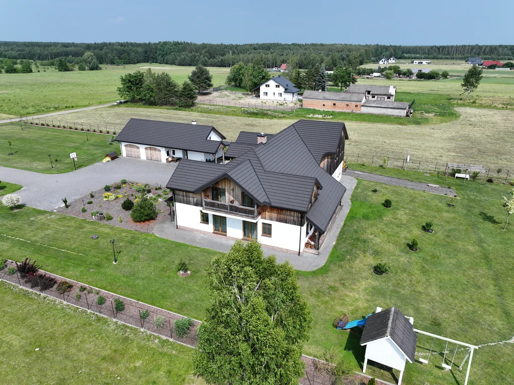 Widok z drona na dom i dużą działkę na wsi z trawnikiem, podjazdem i okolicznymi polami
