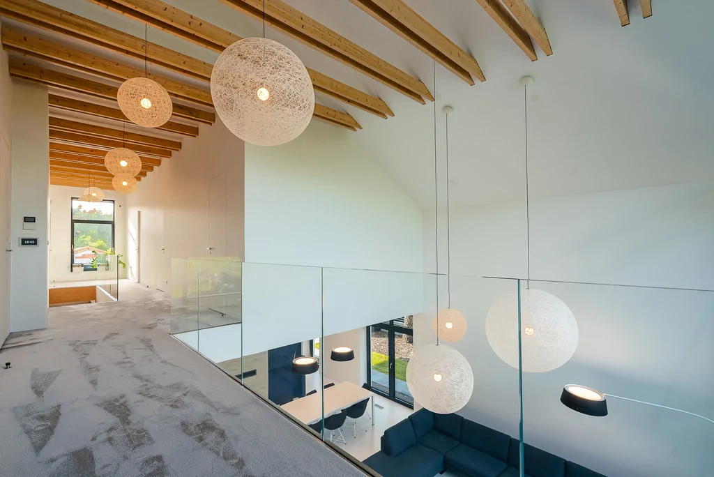 Antresola i korytarz z przeszkloną balustradą oraz dekoracyjnymi lampami kulami.