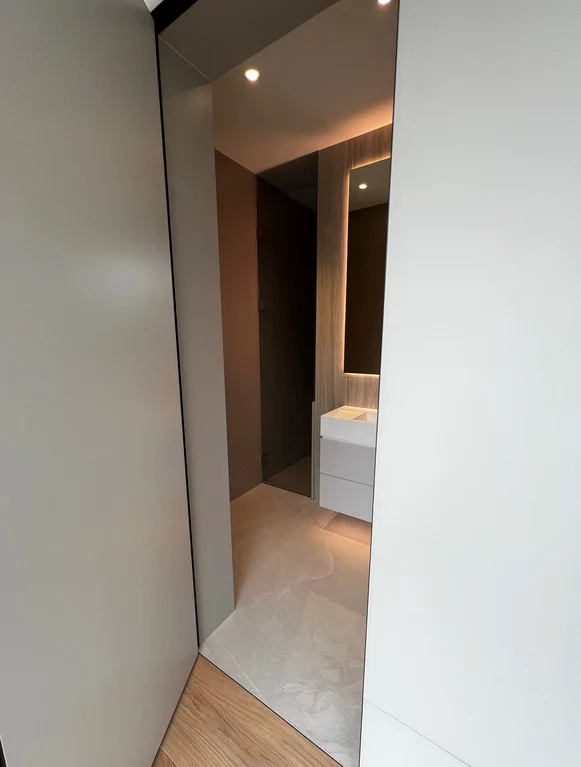 Łazienka: podświetlane lustro, wisząca szafka z umywalką i szklana kabina prysznicowa.