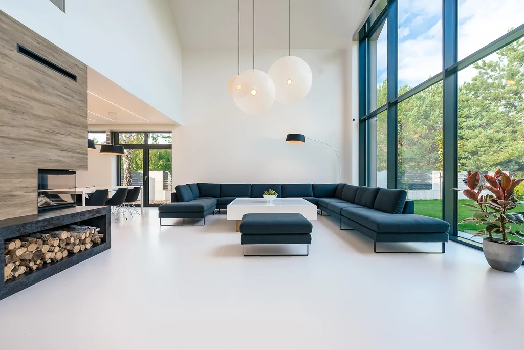 Salon z narożną sofą, wysokim przeszkleniem i kominkiem w nowoczesnym wnętrzu.