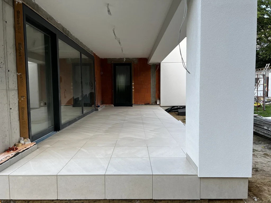 Zadaszony taras nowoczesnego domu w Podkowie Leśnej z dużymi przeszkleniami i jasną posadzką