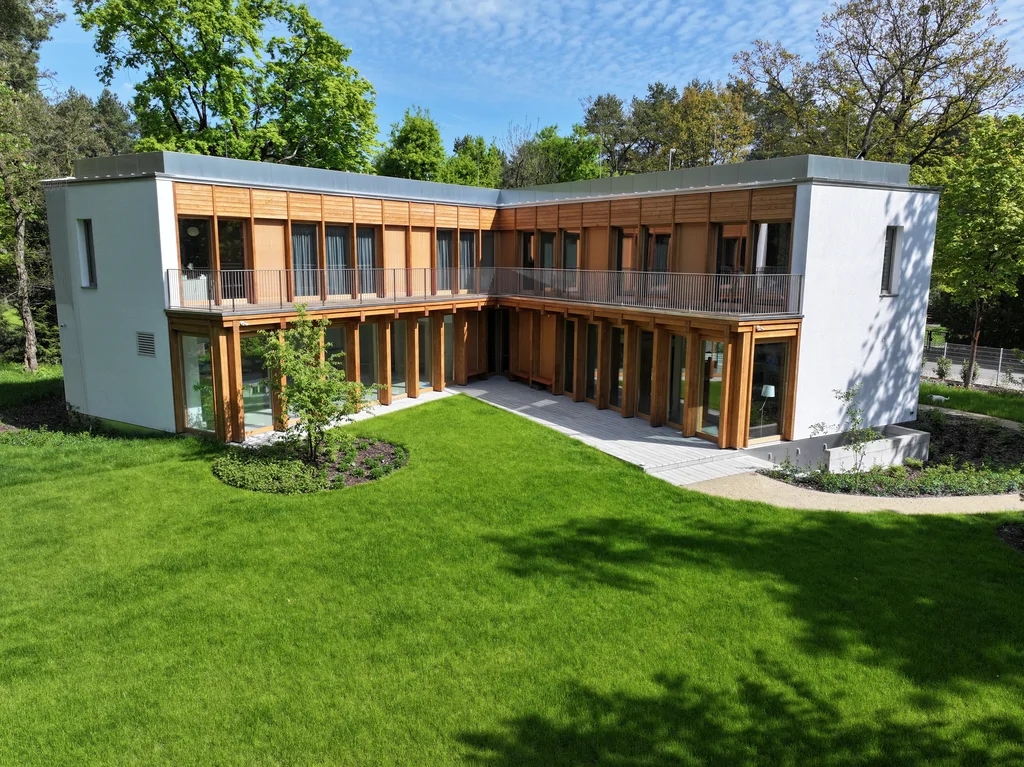 Ujęcie z drona na wewnętrzny ogród i narożną bryłę domu z drewnianymi słupami, balkonem i zielonym dziedzińcem