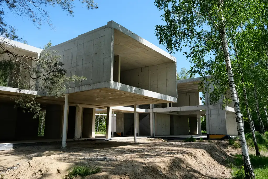 Nowoczesna bryła domu z betonu architektonicznego na etapie stanu surowego w leśnym otoczeniu.