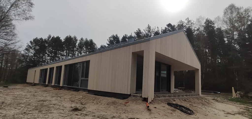 Widok ogólny budynku parterowego: podcień tarasowy, przeszklenia i elewacja drewniana