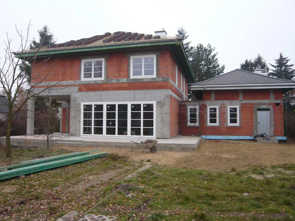 elewacja z dużymi przeszkleniami oraz budynek garażowy z dachem w trakcie prac