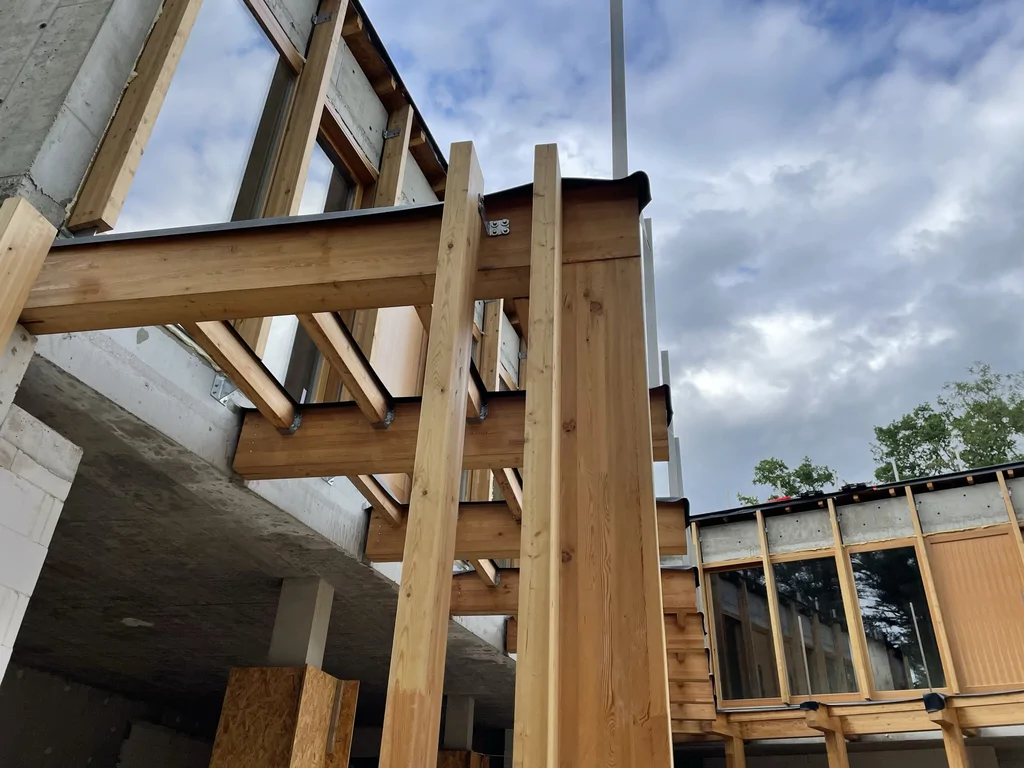 Widok od dołu na drewnianą konstrukcję pergoli i połączenia belek przy elewacji domu jednorodzinnego