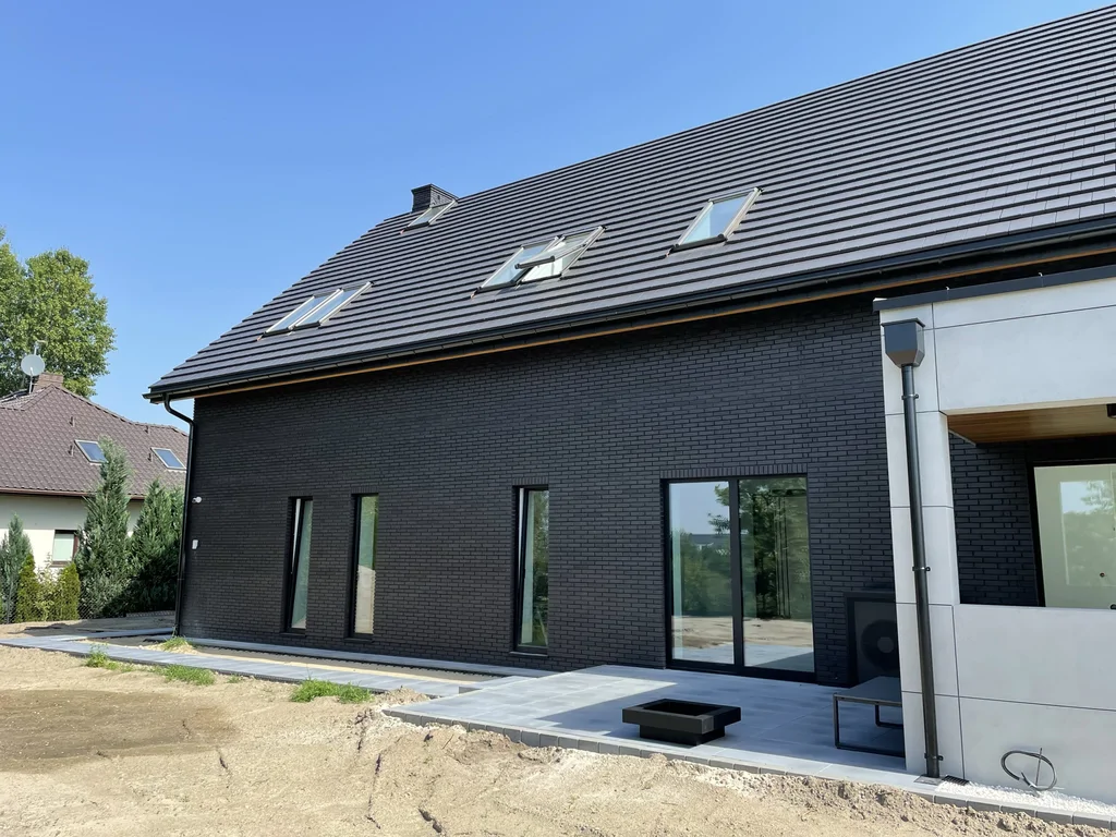 Długa elewacja boczna – czarna cegła, wąskie okna pionowe, opaska tarasowa