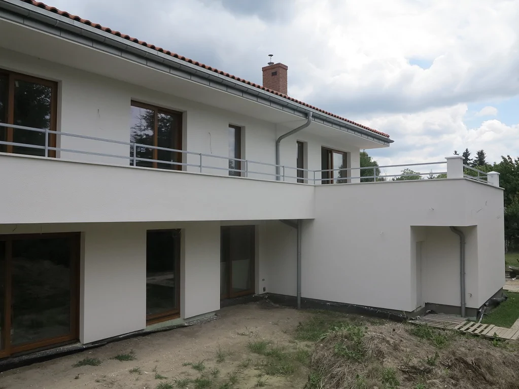 Budowa domu jednorodzinnego, widok z zewnątrz na wykonaną elewację z barierkami na tarasach i balkonach, ciemna stolarka okienna