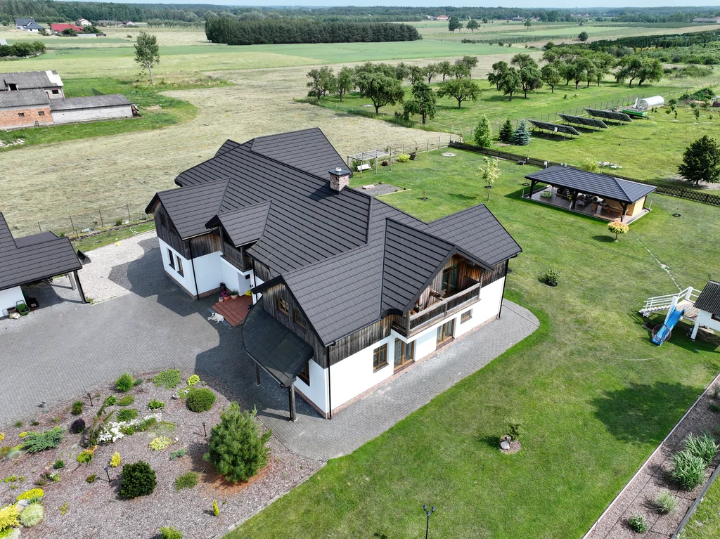 Widok z drona na dom od strony ogrodu z rabatami oraz widoczną altaną i elementami małej architektury na działce