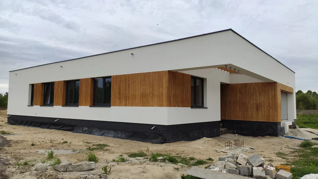 Budynek w stanie deweloperskim, ciemna stolarka okienna, jasna elewacja i elementy okładzina imitująca drewno 