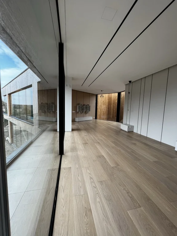 Ujęcie z krawędzi przeszklenia pokazuje relację wnętrza z tarasem i otoczeniem. Lekka, nowoczesna kompozycja.