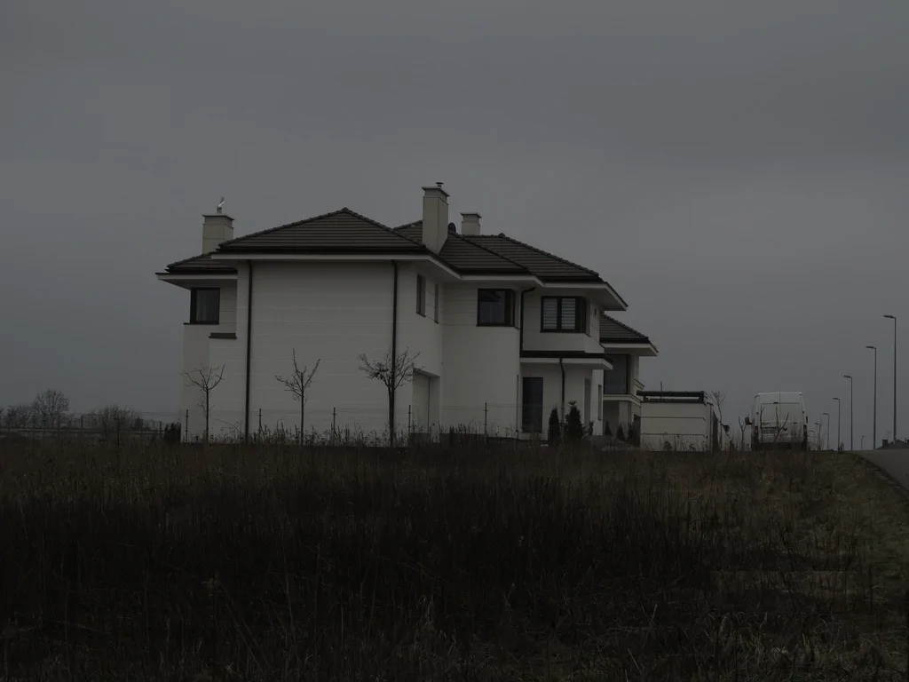 Gotowy dom jednorodzinny z ciemnym dachem, widok z boku przy pochmurnej pogodzie