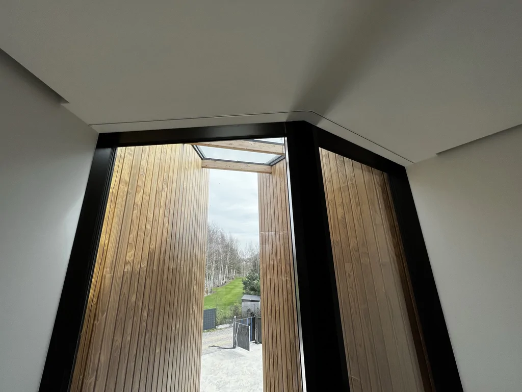 Wysokie przeszklenie w drewnianej wnęce z doświetleniem z góry i czarnymi ramami.